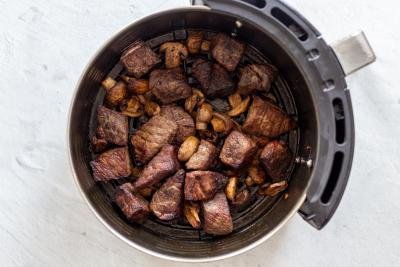 steak bites with mushrooms in an air fryer basket