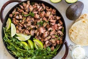 Sliced carne asada on the grilling pan with lime and herbs