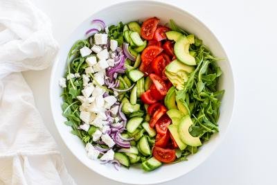 veggies and cheese in a bowl for the Arugula avocado tomato and cucumber salad