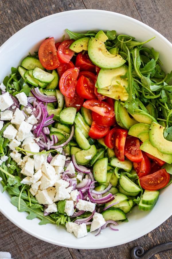 All the ingredients for Arugula avocado tomato and cucumber salad are lined up in a bowl