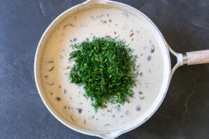 dill added to mushroom gravy in a pan