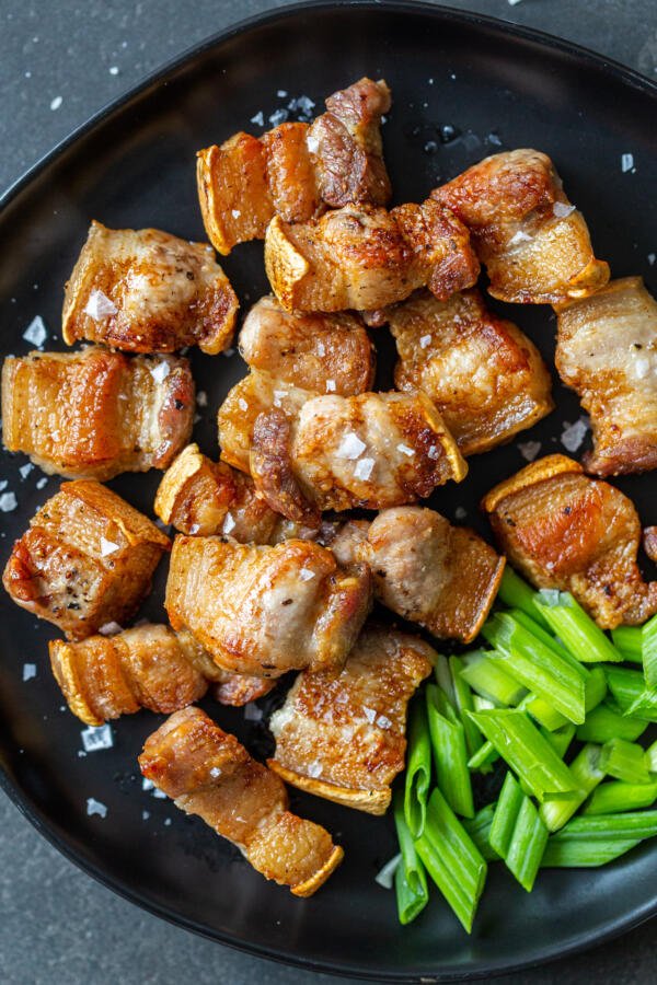 Pork belly bites on a plate with green onions