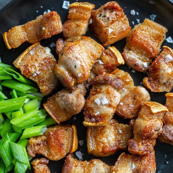 Pork belly bites on a plate with green onions