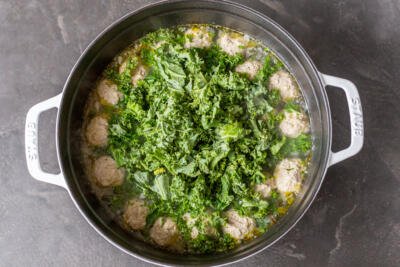 A pot of soup with meatballs and kale