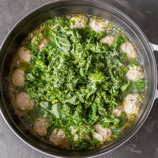 A pot of soup with meatballs and kale