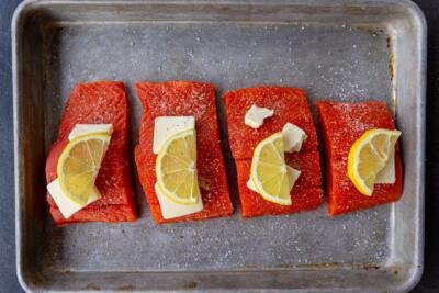 salmon pieces on a baking sheet with butter and lemon