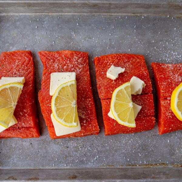 salmon pieces on a baking sheet with butter and lemon