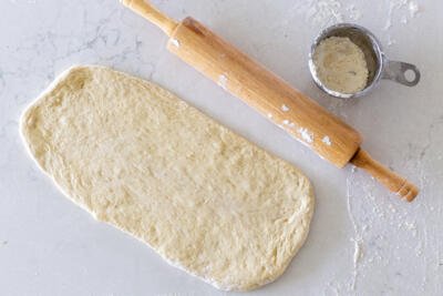 Rolled out flatbread dough with rolling pin next to it