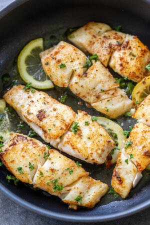 fried halibut in a pan with herbs and lemon