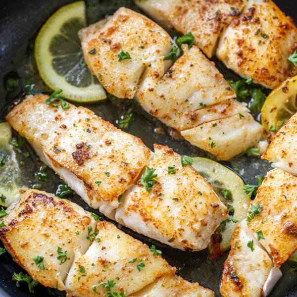 fried halibut in a pan with herbs and lemon