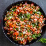 The Classic Pico de Gallo in a bowl with vegetables next to it