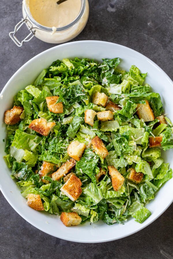 Caesar salad in a bowl with dressing next to it