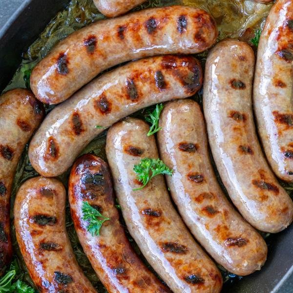 Herbs on top of brats in a baking pan.