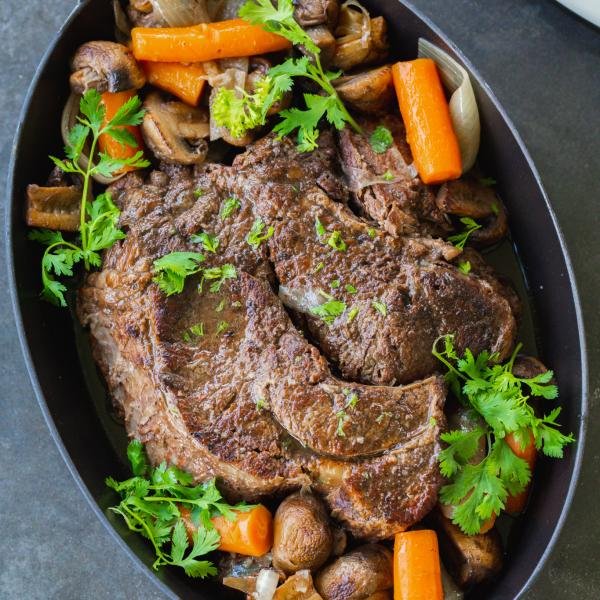 Slow cooked beef roast on a serving tray with veggies.