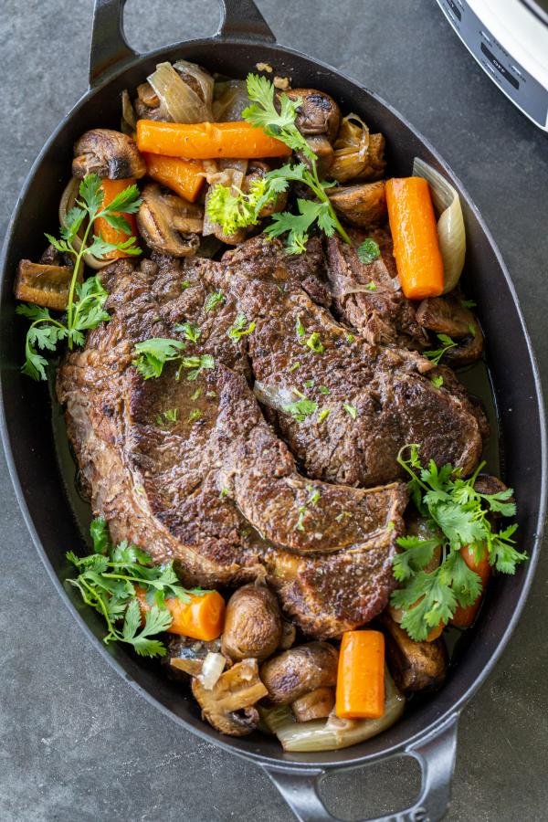 Slow cooked beef roast on a serving tray with veggies. 