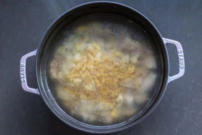 A pot with water, chicken, noodles, potatoes and seasoning.