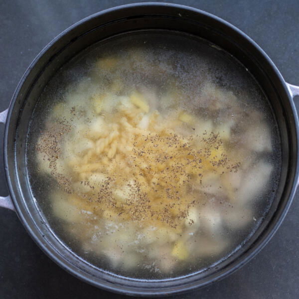 A pot with water, chicken, noodles, potatoes and seasoning.