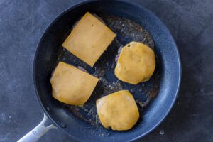Beef patties in a pan with cheese on top,