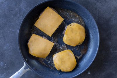 Beef patties in a pan with cheese on top,