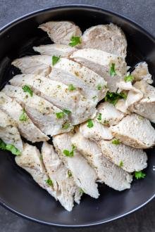Cooked chicken breast in a bowl with herbs and seasoning