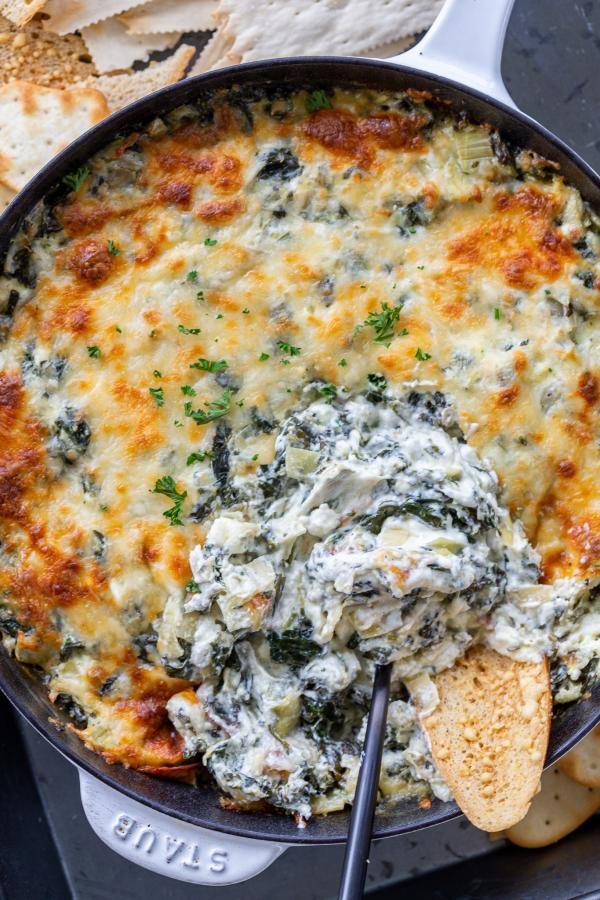 Baked spinach dip in a pan with crackers dipped in