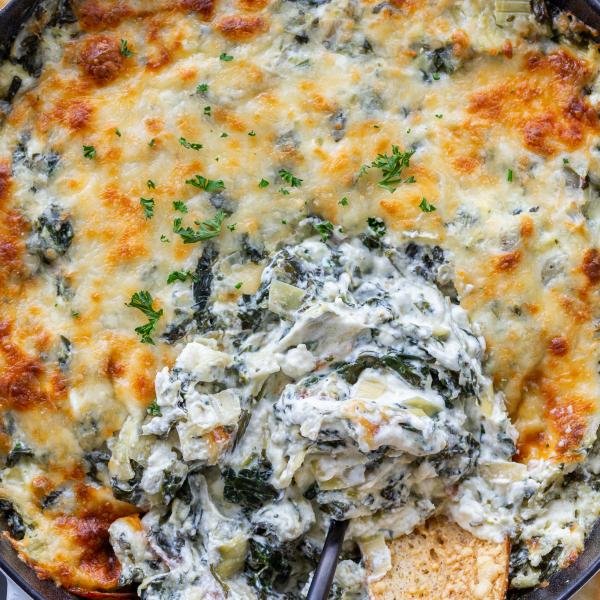 Baked spinach dip in a pan with crackers dipped in