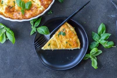 A slice of crustless quiche on a plate with basil around it.