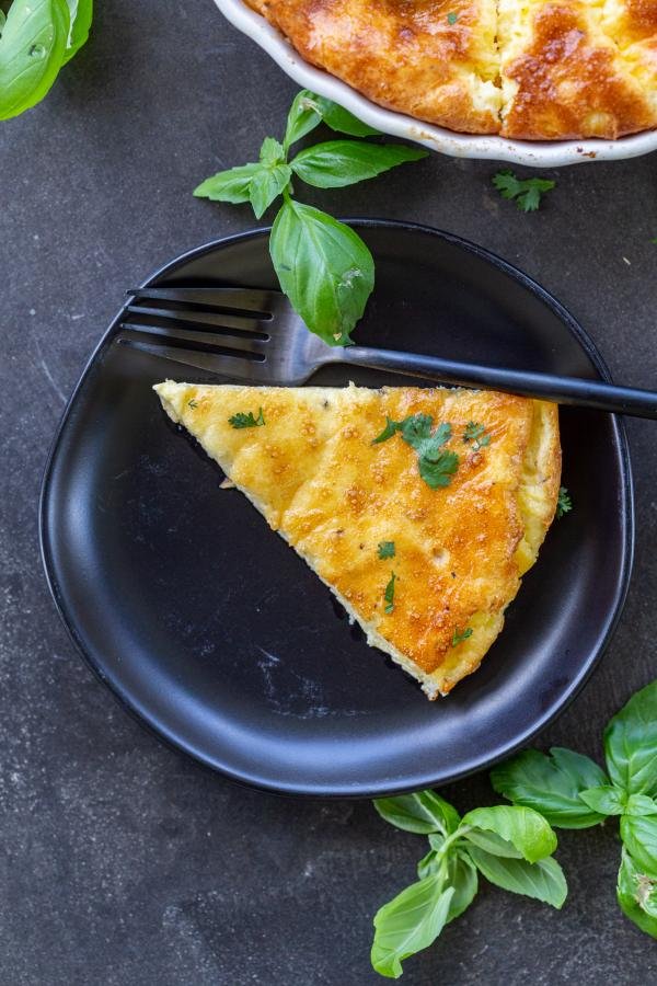 A slice of crustless quiche on a plate with basil around it. 