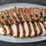 Grilled pork tenderloin sliced up on a plate with herbs on top.