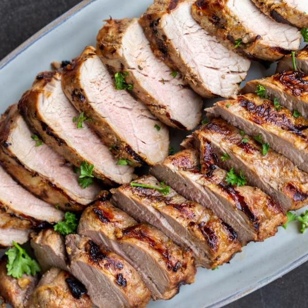 Grilled pork tenderloin sliced up on a plate with herbs on top.