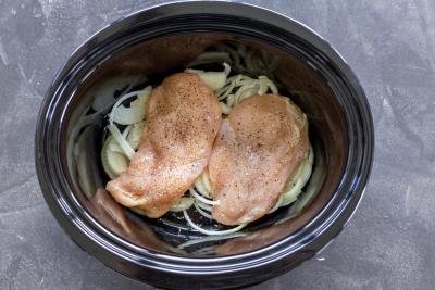 Seasoned chicken and onion in a crock pot.