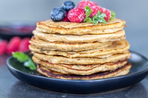 A pile of banana oatmeal pancakes on a plate with fruit.