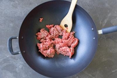 Raw ground beef in a wok cooking.