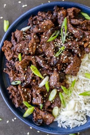 Korean beef bulgogi on a plate with rice and garnish of green onion.