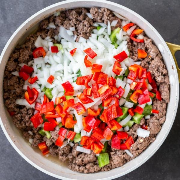 Veggies added to the ground beef in a pan.