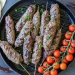 Beef Kafta Kabob on a pan with tomatoes on a tray.