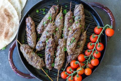 Beef Kafta Kabob on a pan with tomatoes on a tray.