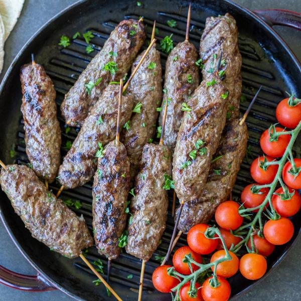 Beef Kafta Kabob on a pan with tomatoes on a tray.
