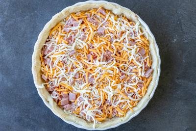 Quiche crust, cheese and ham in a pan.