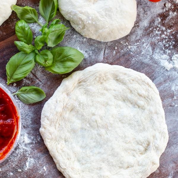 Pizza dough on a tray with toppings next to it.