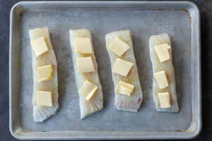 Halibut with seasoning and butter on a baking sheet.