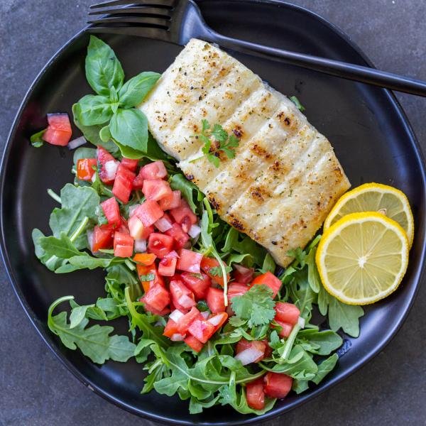 Grilled halibut on a pan with salad and lemon.