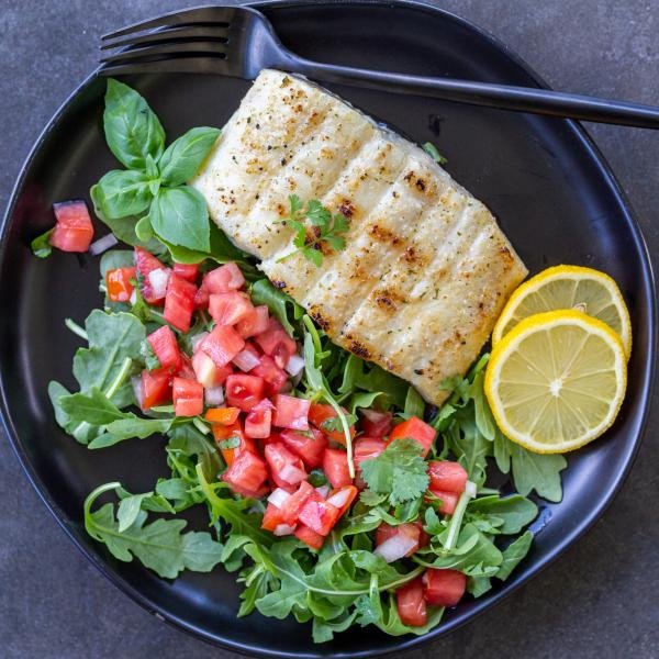 Grilled halibut on a pan with salad and lemon.