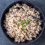 Cooked Farro in a bowl with herbs and a spoon.
