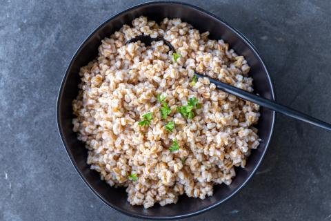 Cooked Farro in a bowl with herbs and a spoon.