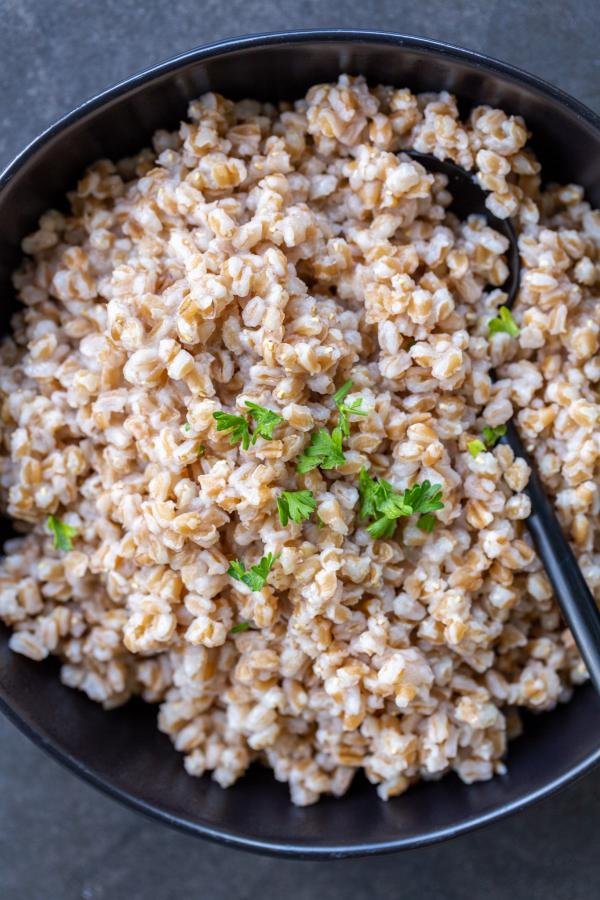 Cooked Farro in a bowl with herbs and a spoon.