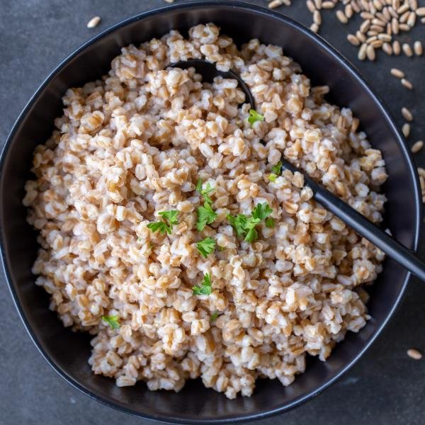 Cooked Farro in a bowl with herbs and a spoon.