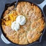 Southern Peach Cobbler in a pan with spoon and ice cream.