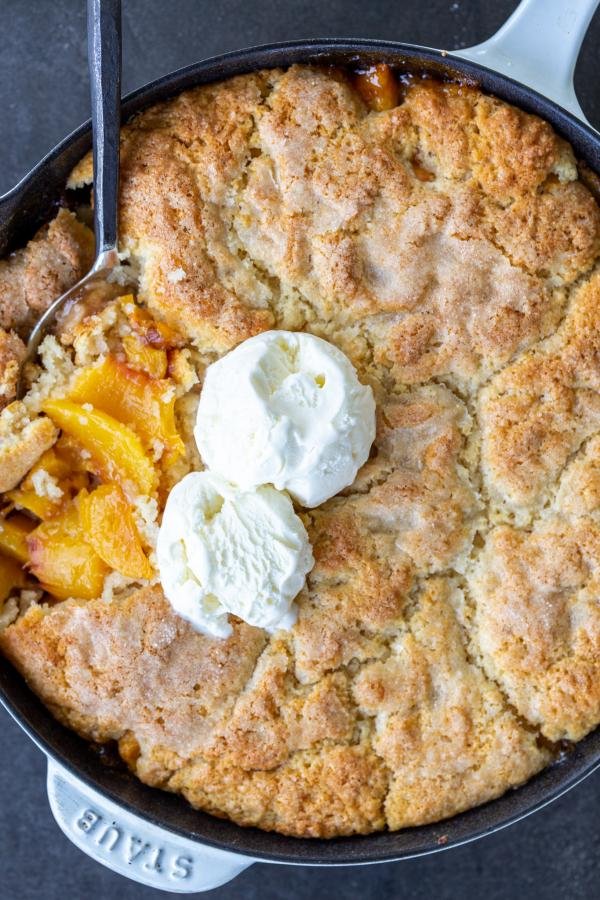 Southern Peach Cobbler in a pan with spoon and ice cream.