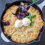 Cherry Cobbler in a pan with ice cream and herbs on top.